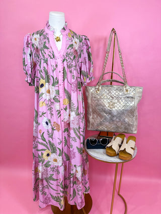 Short sleeve pink midi dress with a button front, soft ruffle neckline, subtle puff sleeves, and a tiered skirt finished in a dreamy pink floral print. 
