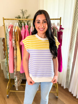 Woman wearing a striped pastel yellow, purple, and white textured blouse with light denim pants