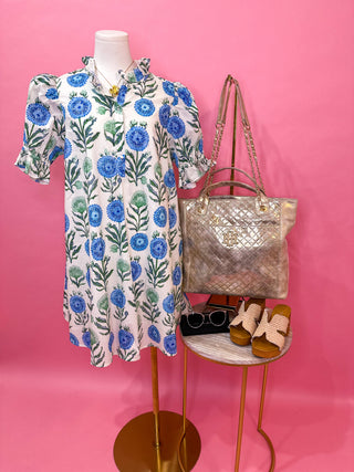 Short sleeve blue mini dress with a ruffle neckline, button front detail, flutter sleeves, and a flowy silhouette finished in a blue and green floral print with a tie-back detail