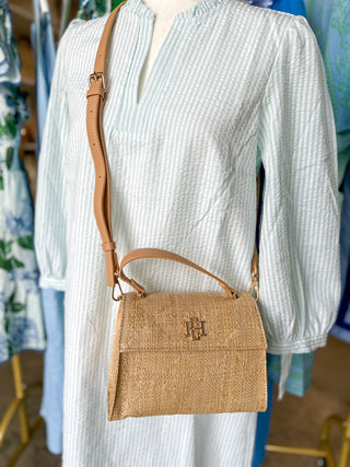Mannequin wearing a white outfit with a natural, woven, straw handbag featuring a Caroline Hill logo. 