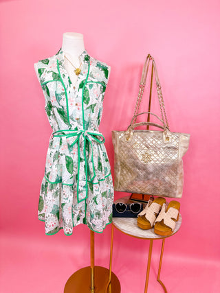 Sleeveless mini dress with a collared neckline, button front, adjustable tie waist, contrast piping details, and a tiered skirt in a bold green floral print