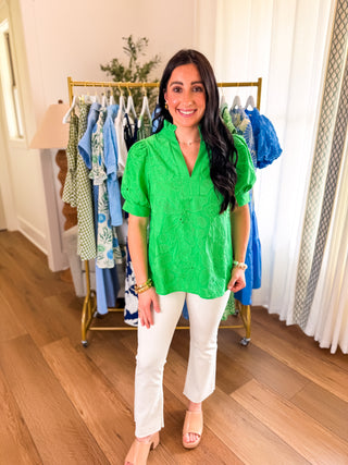 Woman wearing a kelly green  embroidered floral v-neck top paired with white denim pants