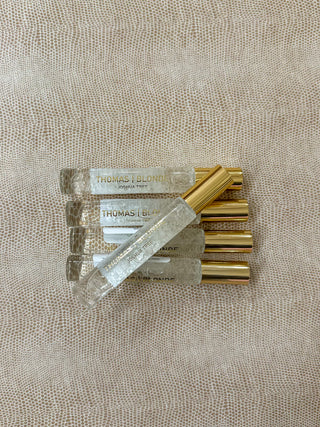 Five small clear glass perfume roller bottles with gold caps and gold letters reading THOMAS BLONDE