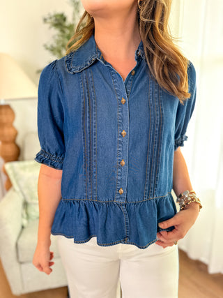 Woman wearing a boutique blue denim functional button-down blouse with ruffled details